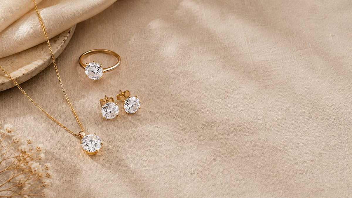 Round-stone pendant, stud earrings and solitaire ring on beige fabric